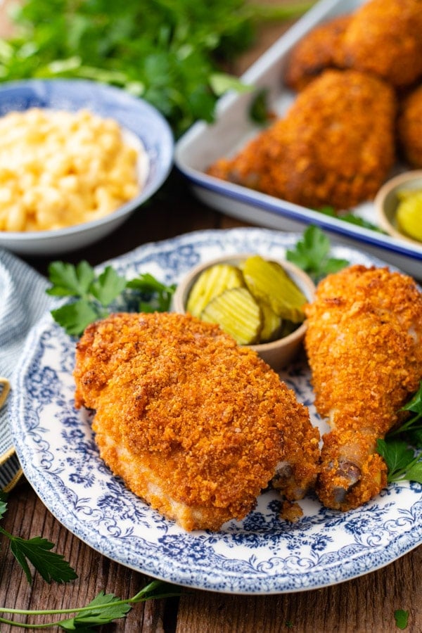 Two pieces of crispy oven-fried Ranch chicken - one bone-in thigh and one drumstick - served on a plate with a small dish of pickles.