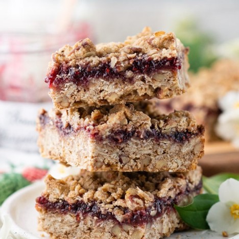 Close up side shot of a stack of three raspberry crumble bars on a white plate