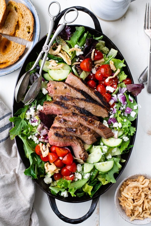 Overhead image of grilled steak salad recipe on a large serving platter with a side of bread