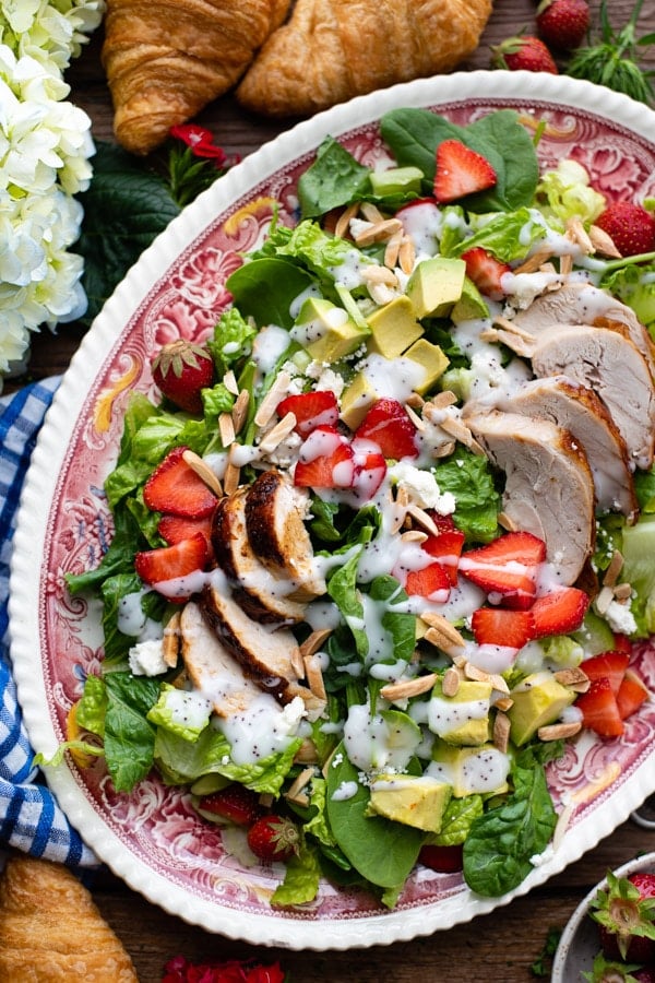 Avocado strawberry chicken salad on a red and white plate with poppy seed dressing