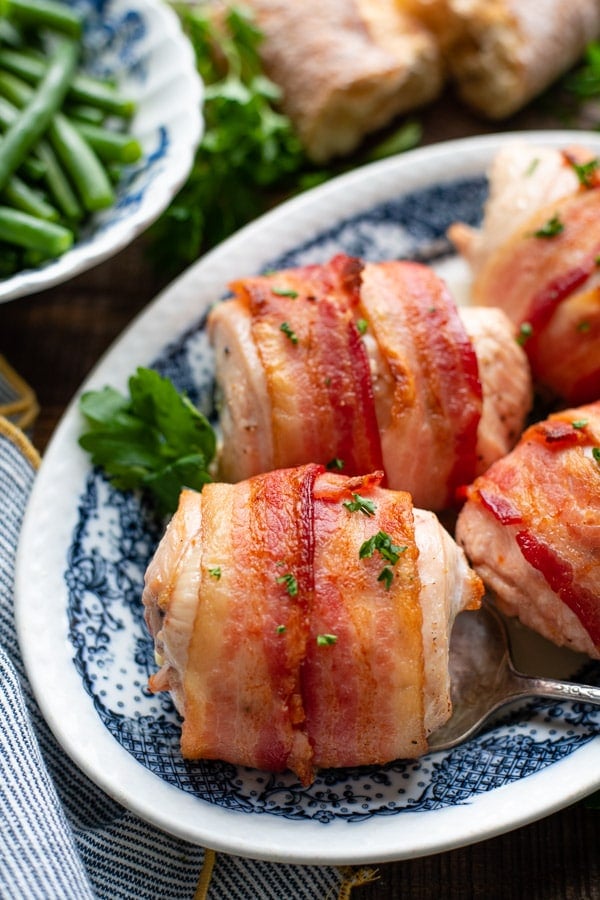 Close up front shot of stuffed bacon wrapped chicken on a blue and white platter