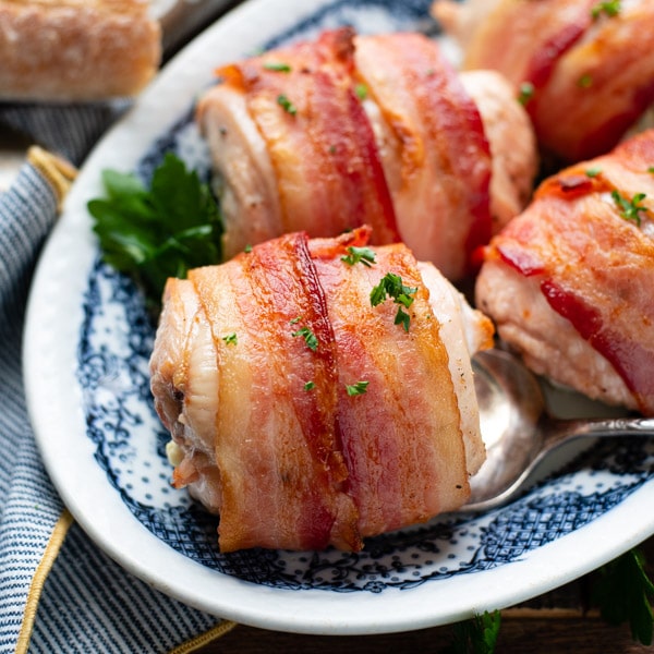 Square image of a plate of bacon wrapped cream cheese stuffed chicken on a plate
