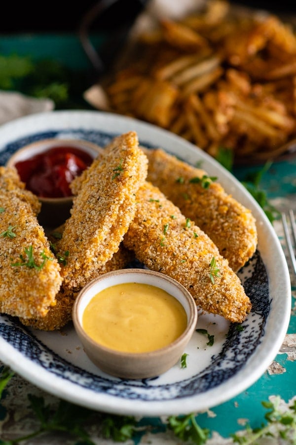 Close up shot of a plate of the best baked chicken tenders recipe served with a side of honey mustard for dipping