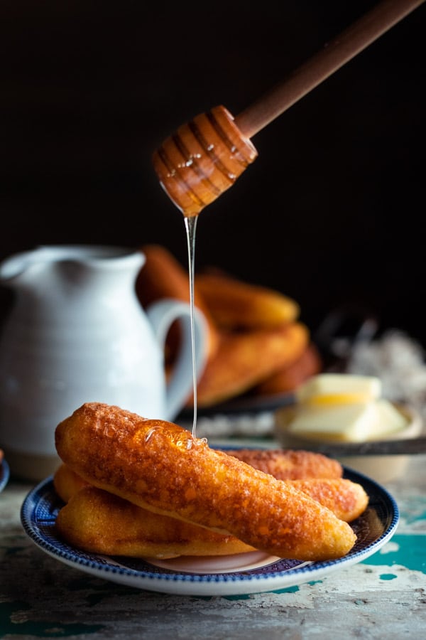 Drizzling honey on a plate of cast iron corn sticks