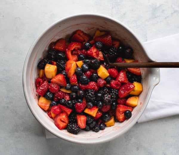 An overhead shot of a mixed fruit salad in a bowl with a wooden spoon, dressed with a sweet vanilla fruit salad dressing.