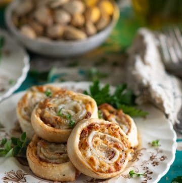 Close up side shot of a plate of baked Italian Pinwheels with a bowl of nuts in the background