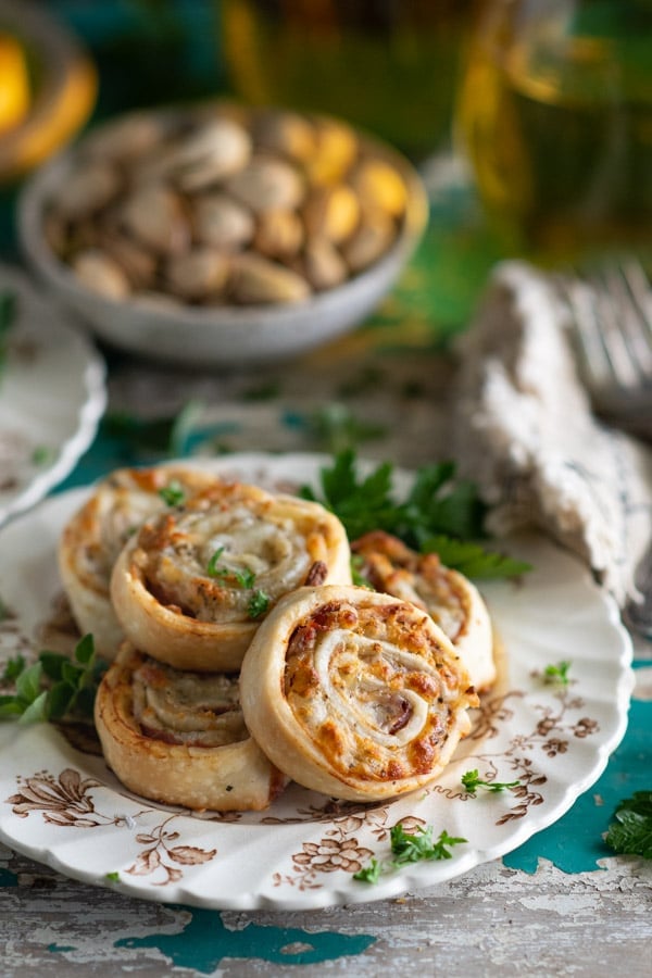 Close up side shot of a plate of baked Italian Pinwheels with a bowl of nuts in the background