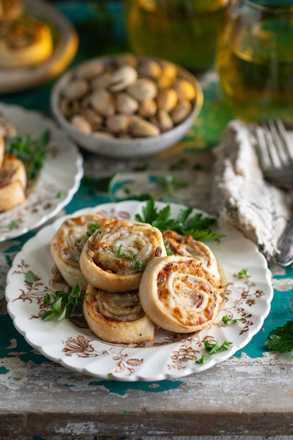 Side shot of hot Italian pinwheels on a brown and white vintage plate with cocktails in the background