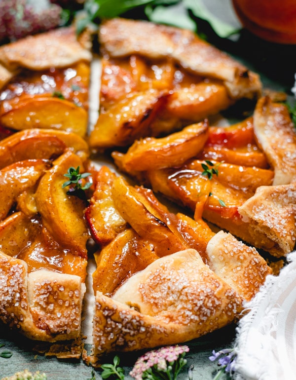 Close up side shot of a rustic peach galette garnished with fresh thyme
