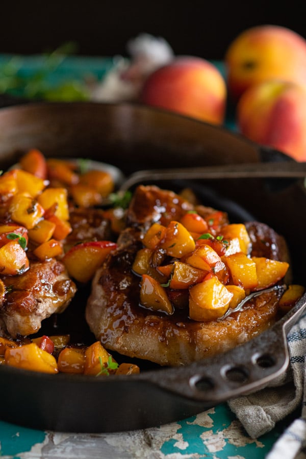 Close up side shot of thick cut pan fried pork chops in a cast iron skillet with fresh peach sauce on top