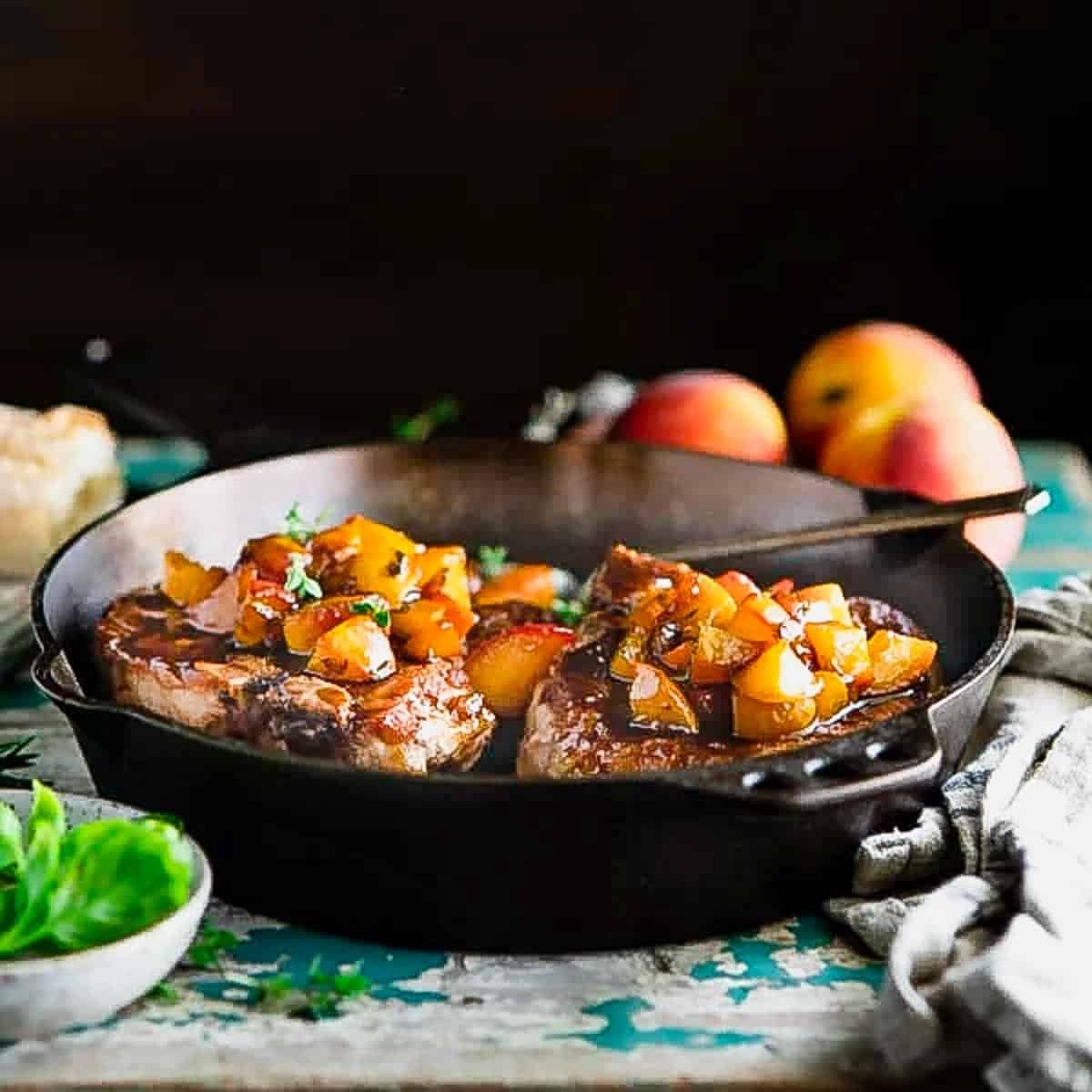 Square side shot of pan fried pork chops with peach sauce in a cast iron skillet.