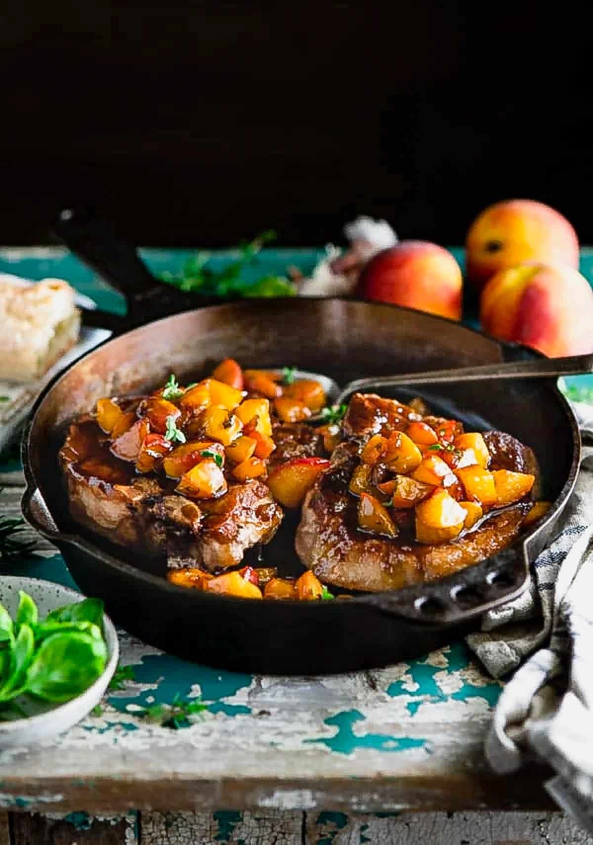 Side shot of a cast iron skillet full of pork chops and peach sauce.