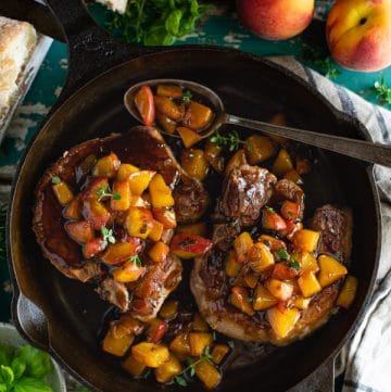 Overhead shot of a cast iron skillet with fried pork chops and peach sauce.