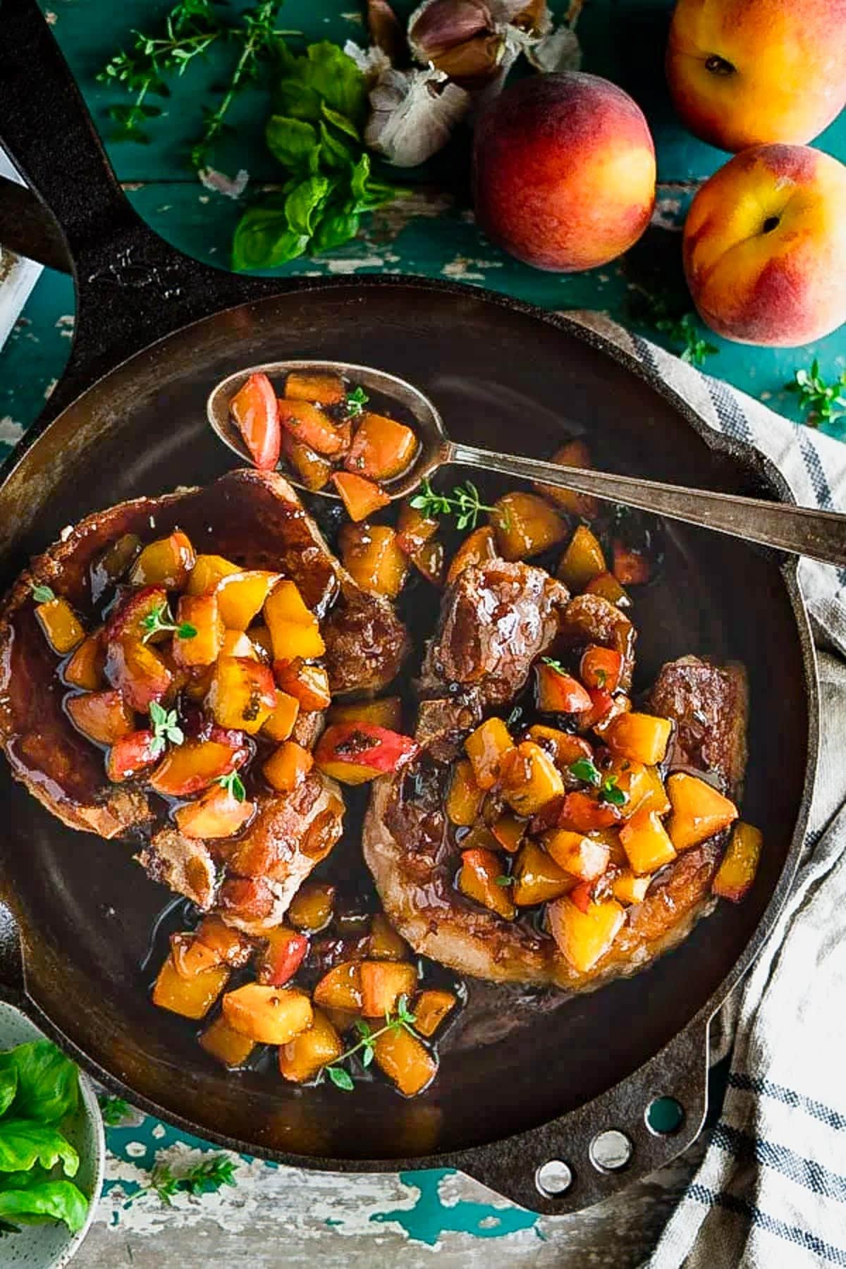 Close overhead image of pan fried pork chops with peach sauce in a cast iron skillet.