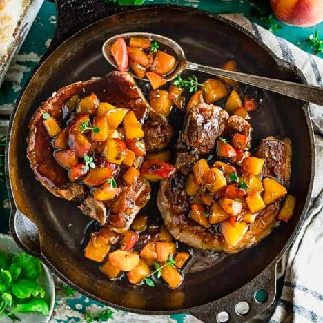 Square overhead image of pan fried pork chops with peach sauce in a cast iron skillet.
