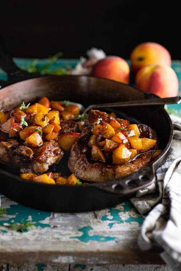 Close up side shot of cast iron skillet with pork chops and peaches on a rustic blue table