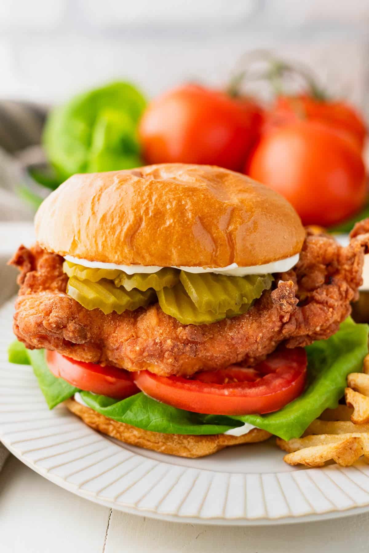 Close up side shot of a white plate with a fried chicken sandwich on it.