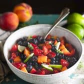 Side shot of a bowl of easy fruit salad with vanilla pudding dressing on a turquoise table.