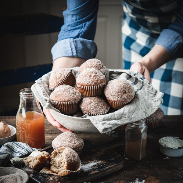 Close up square shot of hands holding a bowl of apple cider muffins