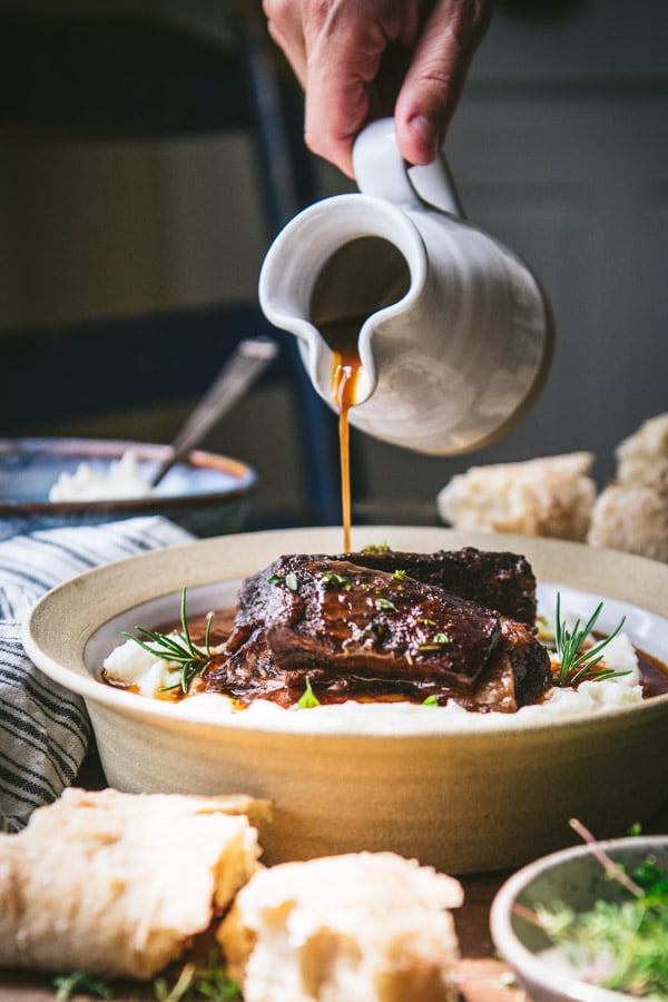 Pouring red wine sauce over braised beef short ribs
