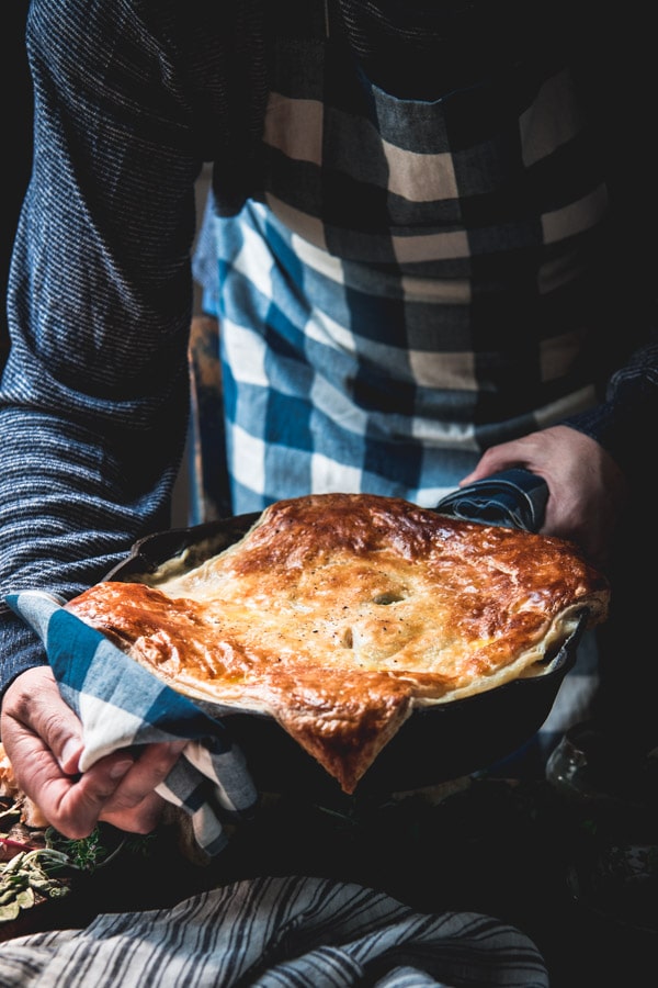 Hands holding a pan of chicken pot pie topped with puff pastry