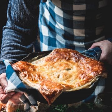 Hands holding a pan of creamy chicken pot pie with puff pastry