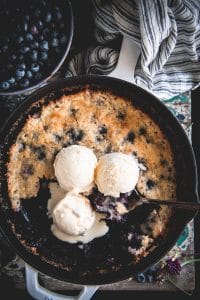Close up shot of a skillet blueberry cobbler with three scoops of vanilla ice cream on top