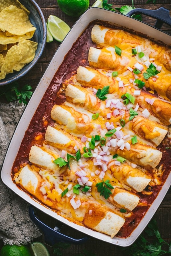 Overhead image of a pan of easy chicken enchiladas on a wooden table with a side of chips and salsa