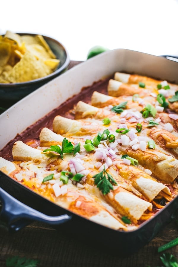 A casserole dish filled with freshly baked chicken enchiladas topped with melted shredded cheese and garnished with green and red onions and fresh chopped cilantro.