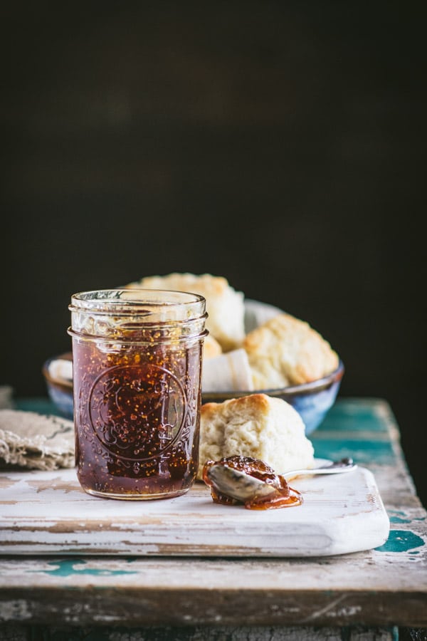 Side shot of a jar of fresh fig preserves with a bowl of biscuits