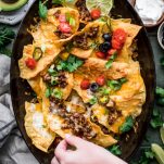 Overhead shot of a hand reaching and picking up simple homemade nachos recipe on a tray