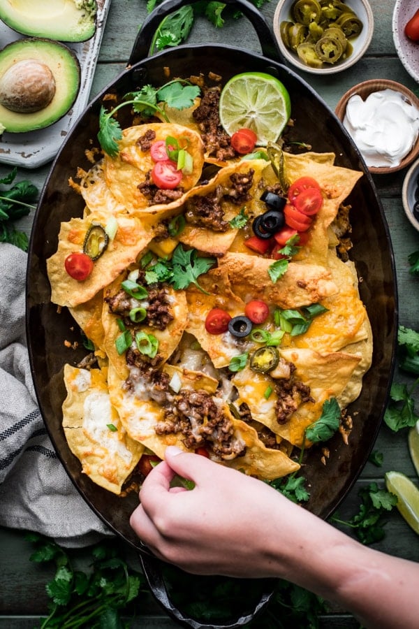 Overhead shot of a hand reaching and picking up simple homemade nachos recipe on a tray