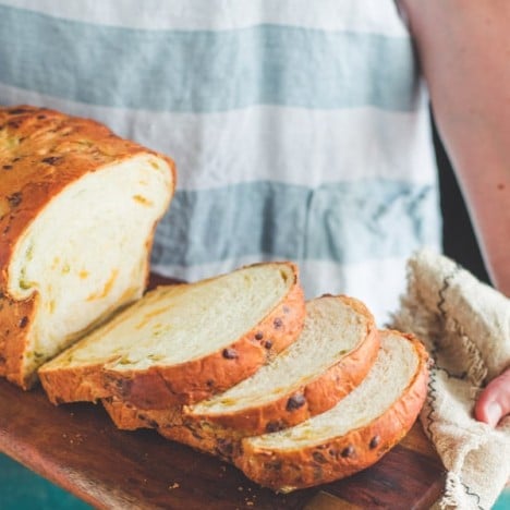 Hands holding jalapeno cheddar bread sliced on a wooden board