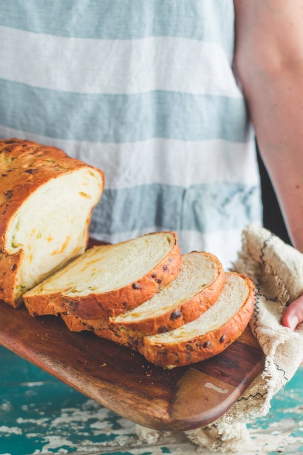 Hands holding jalapeno cheddar bread sliced on a wooden board