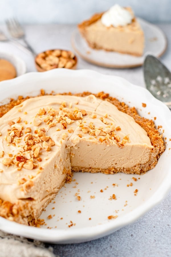 An old fashioned peanut butter pie in a ceramic white pie dish with two slices cut out.