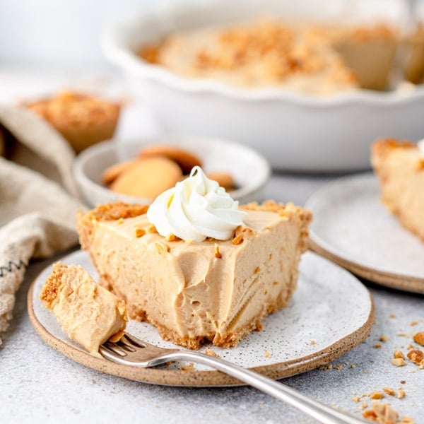 A slice of creamy old fashioned peanut butter pie, served on a plate and topped with a dollop of whipped cream. A silver fork sits on the plate holding a bite of pie.
