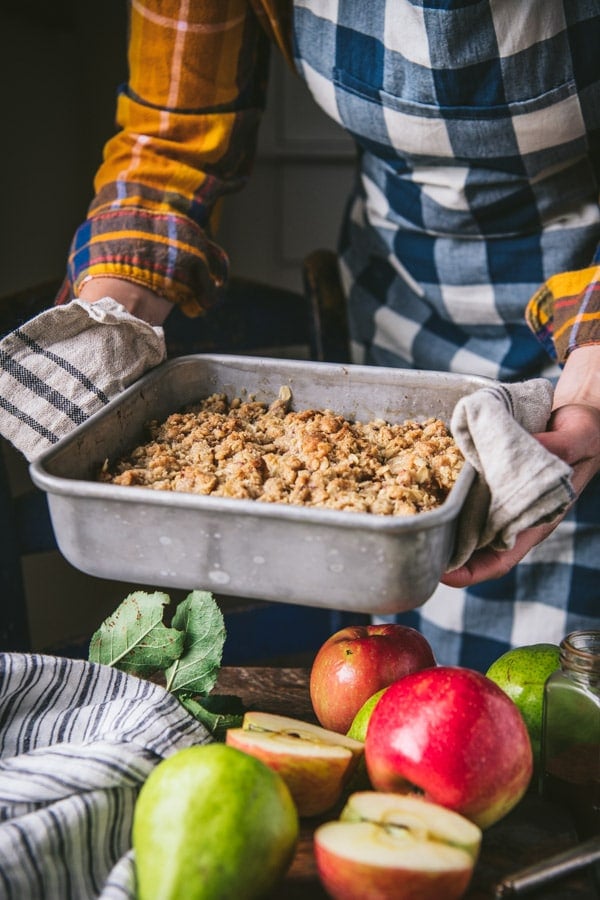 Hands holding a baked pear crisp with oats