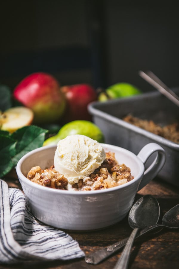 Side shot of an easy pear crisp recipe served in a white bowl with a scoop of vanilla ice cream on top