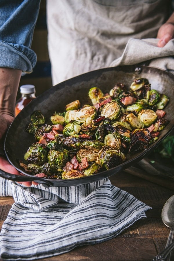 Side shot of hands holding a roasting pan full of roasted brussels sprouts with balsamic