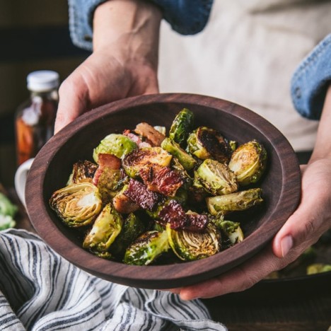 Hands holding a bowl of oven roasted brussels sprouts with balsamic and bacon