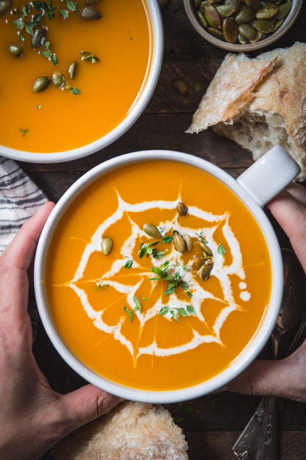 Overhead shot of hands holding a white bowl full of simple butternut squash soup