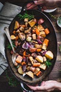 Overhead image of hands holding a pan of balsamic roasted root vegetables on a wooden table
