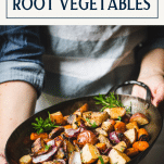 Hands holding a pan of roasted root vegetable medley with text title box at top