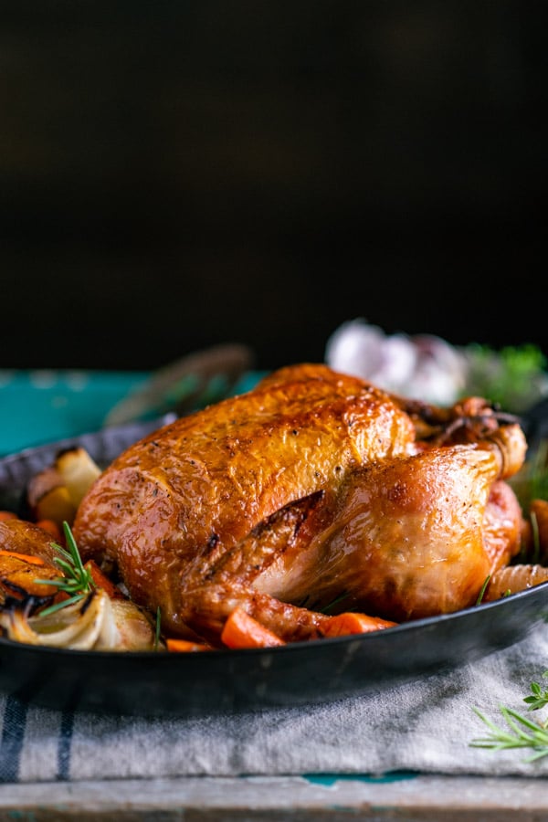 Side shot of oven roasted whole chicken on a pan in front of a dark background