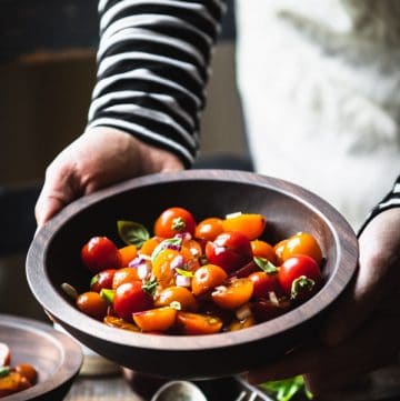 Hands holding a bowl of fresh tomato salad with basil and balsamic
