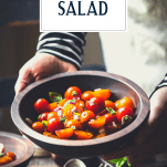 Hands holding a bowl of tomato salad with basil and red onion and text title overlay