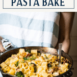 Hands holding a pan of baked pasta with cheese and a text title box at top