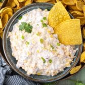 A bowl of creamy cold cheesy corn dip with tortilla chips for scooping.