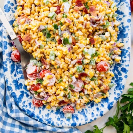 Square overhead shot of a serving platter full of a cold, summer creamy corn salad with tomatoes and bacon.