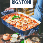 Hands holding a pan of baked rigatoni with text title overlay